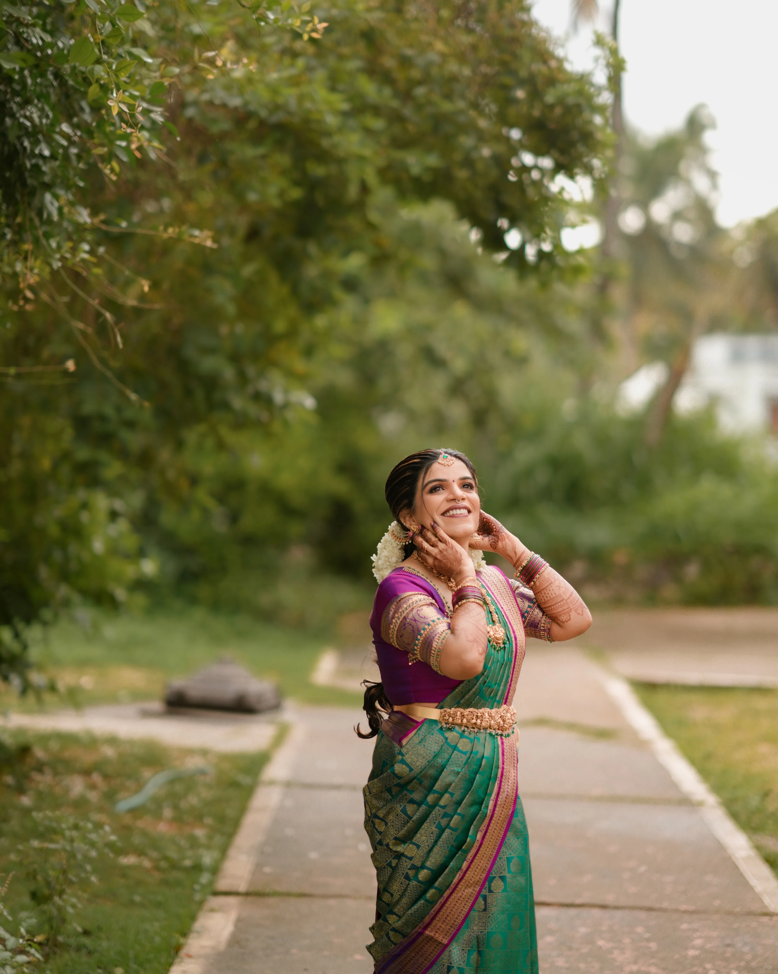 A bride smiling beneath the trees in colorful traditional attire